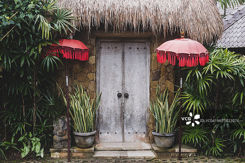 传统巴厘岛房屋的入口，木门，草顶和红色雨伞图片素材