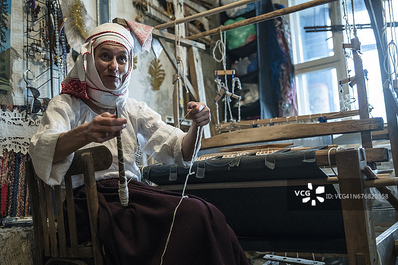 成熟的白俄罗斯妇女穿着传统服装在老式织布机旁纺纱图片素材