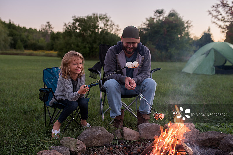 父亲和女儿坐在篝火旁，在火上烤棉花糖图片素材