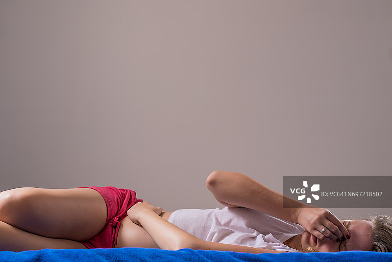 因为肚子痛，女人抱着肚子躺在床上。图片素材