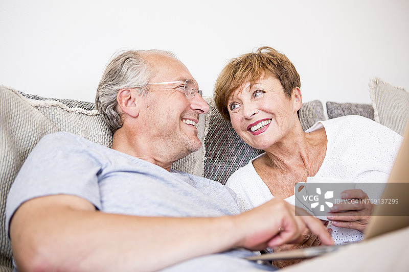 一对快乐的老年夫妇坐在沙发上用笔记本电脑图片素材