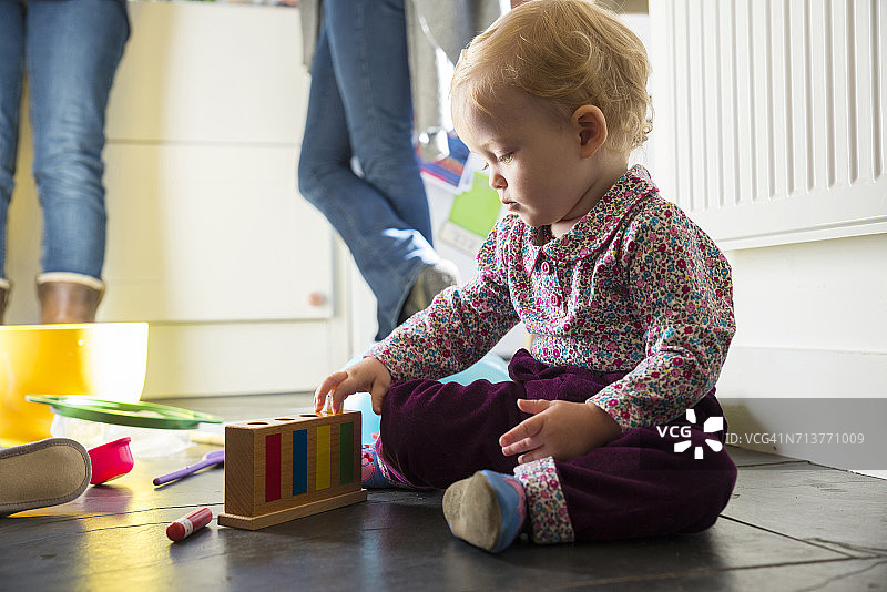 女婴坐在厨房地板上玩玩具图片素材