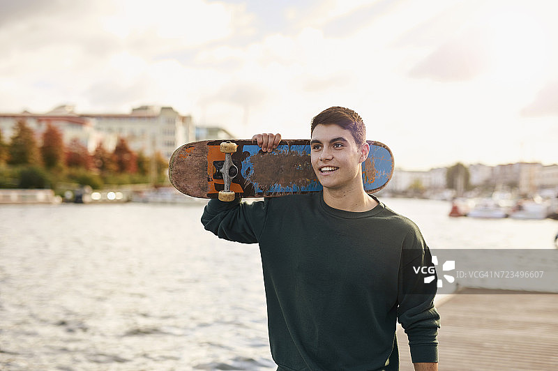 英国布里斯托尔，年轻人扛着滑板走在河边图片素材