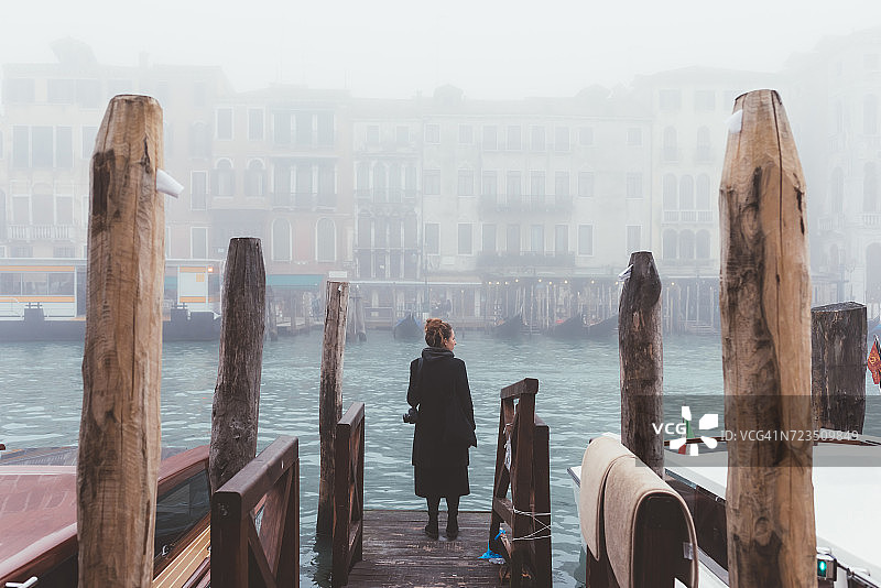 女人从朦胧的运河码头，威尼斯，意大利的后视图图片素材