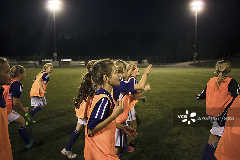 女孩们晚上在灯火通明的足球场上奔跑图片素材