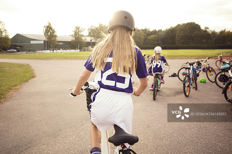 后视图的女孩骑在人行道上的足球场对天空图片素材