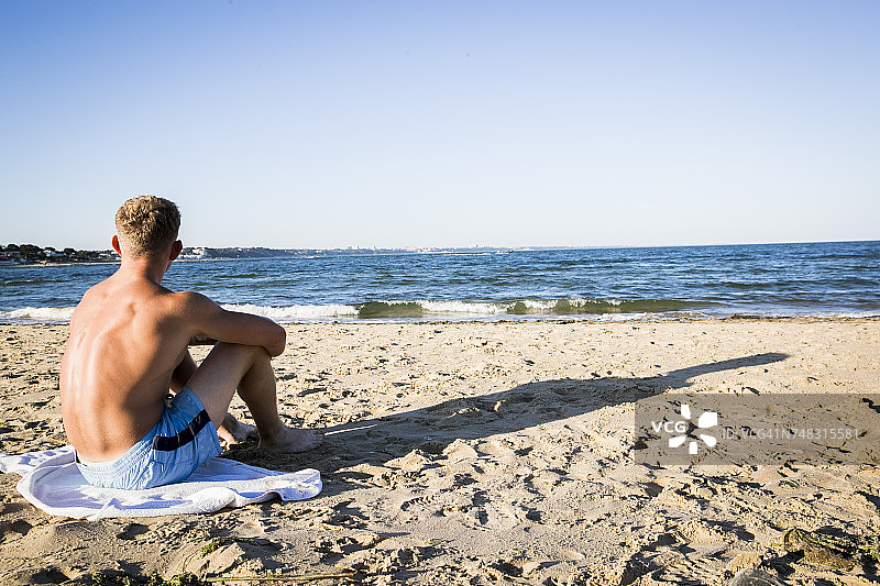 年轻人坐在沙滩上，望着大海图片素材