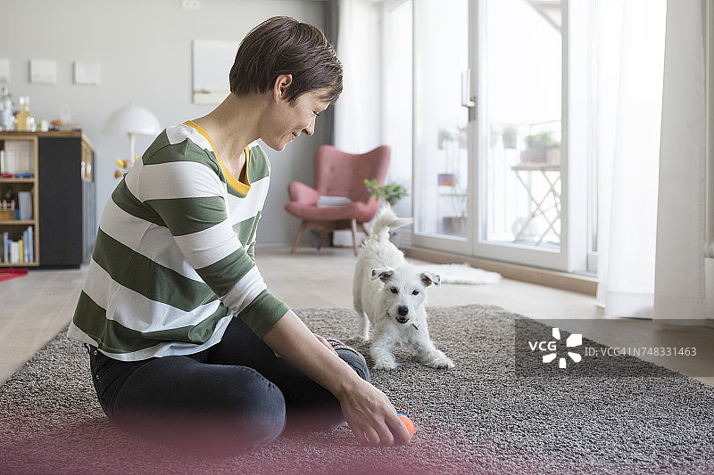 微笑的女人坐在家里的地板上和她的狗玩图片素材