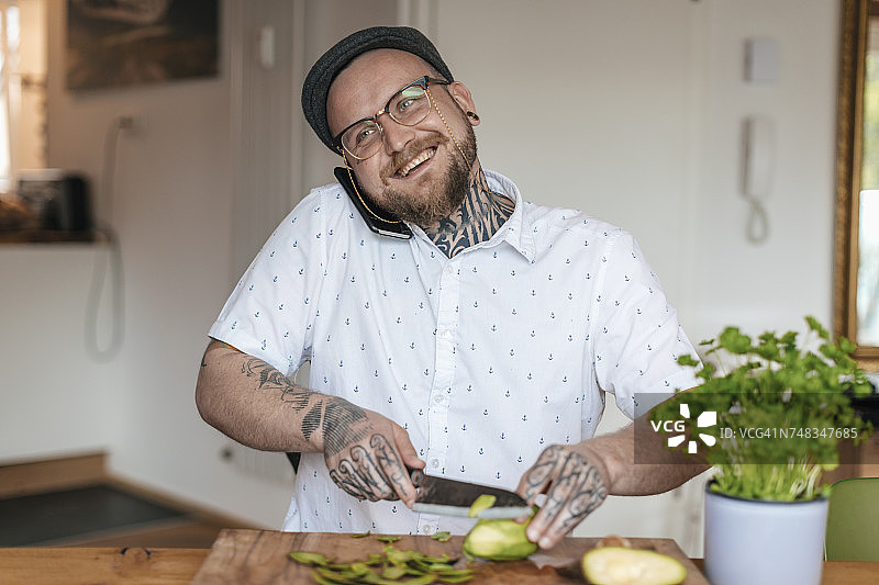 电话里微笑的男人在厨房里切菜图片素材