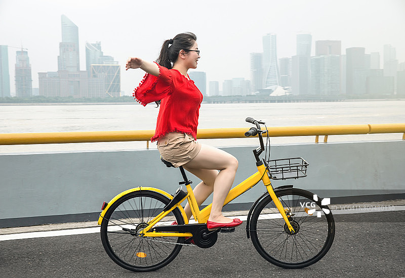 中国杭州，一名年轻女子骑着自行车城市天际线图片素材