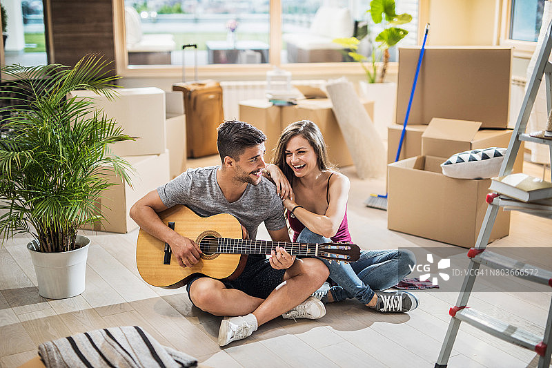 幸福的夫妇在爱享受声吉他在他们的新家。图片素材