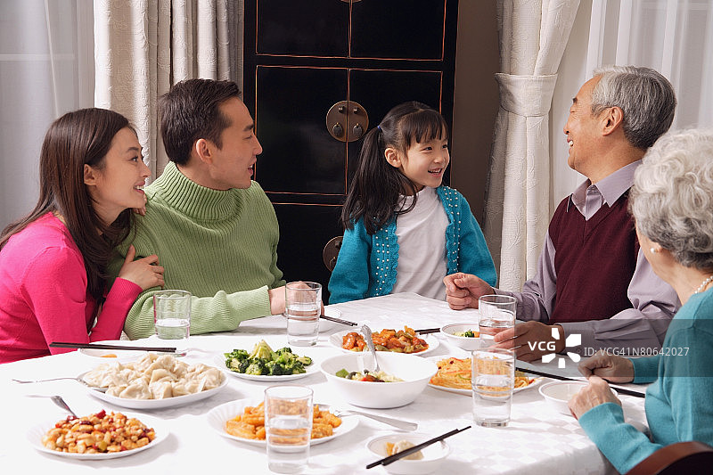 一家人在餐桌上吃传统食物，女孩站在爷爷旁边图片素材
