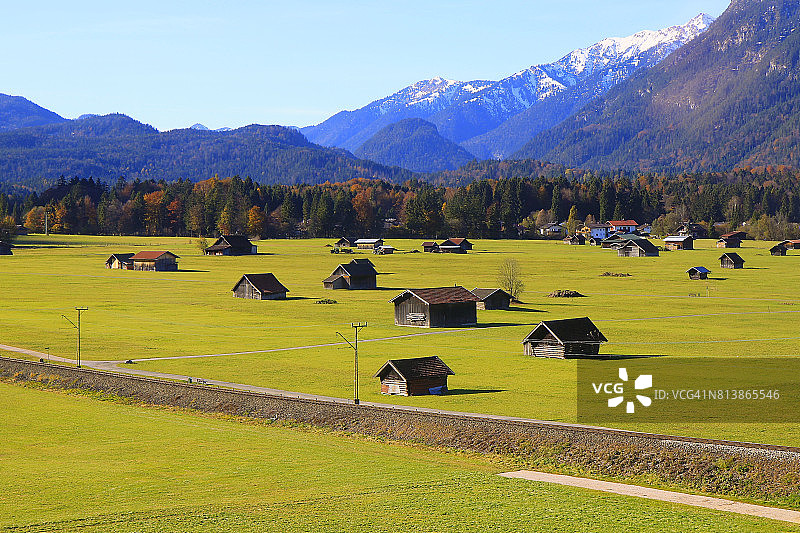 在谷仓农场和小木屋之上，阳光明媚的Garmisch Partenkirchen阿尔卑斯村庄在巴伐利亚阿尔卑斯山从Alpspitze，田园诗般的松树林地秋季景观，雄伟的阿尔卑斯山谷，戏剧性的巴伐利亚德国雪山全景，德国图片素材