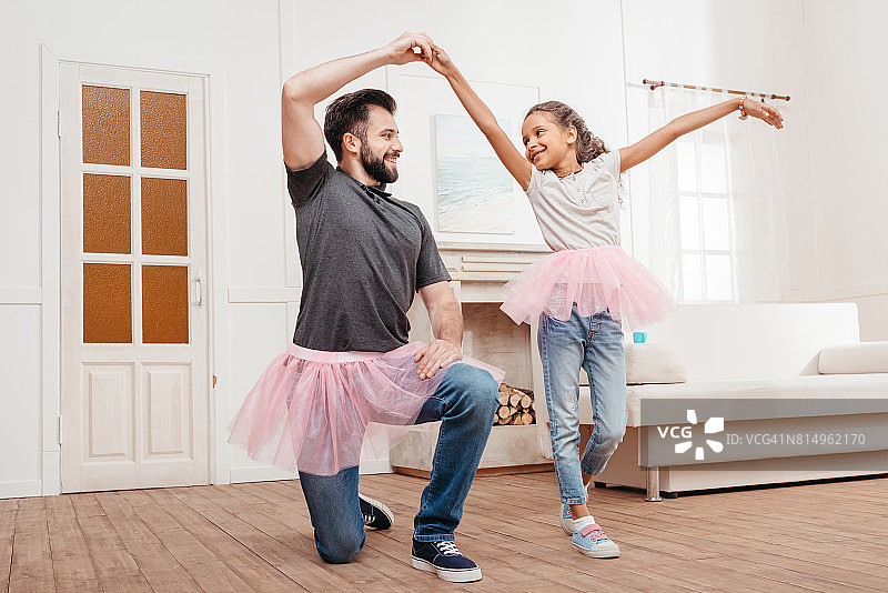 多文化背景的父女穿着粉红色的薄纱短裙在家跳舞图片素材