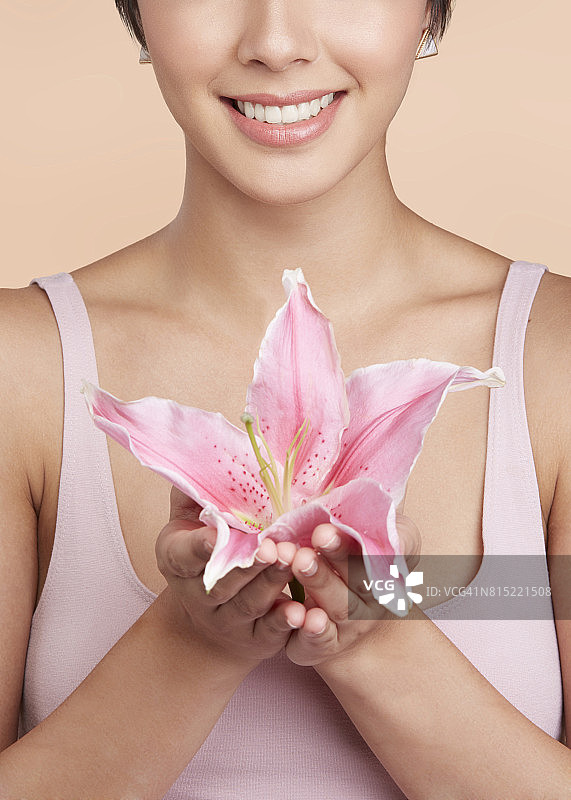 微笑的女人，有闪亮的白牙齿，举着一朵粉红色的花靠近她的胸部图片素材