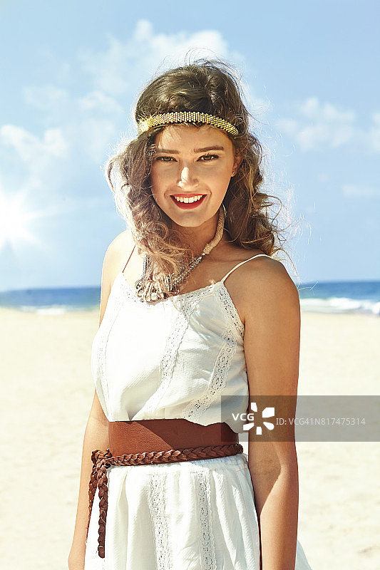 美丽的年轻女子穿着白色的裙子和长发微笑在一个阳光灿烂的日子在海边图片素材