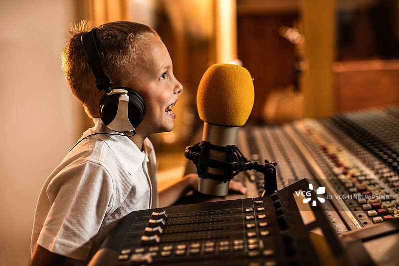 一个快乐的小男孩在电台里对着麦克风说话。图片素材
