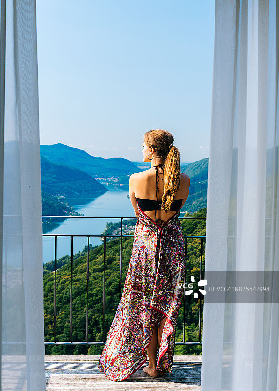 女人在酒店阳台上俯瞰着湖和山图片素材