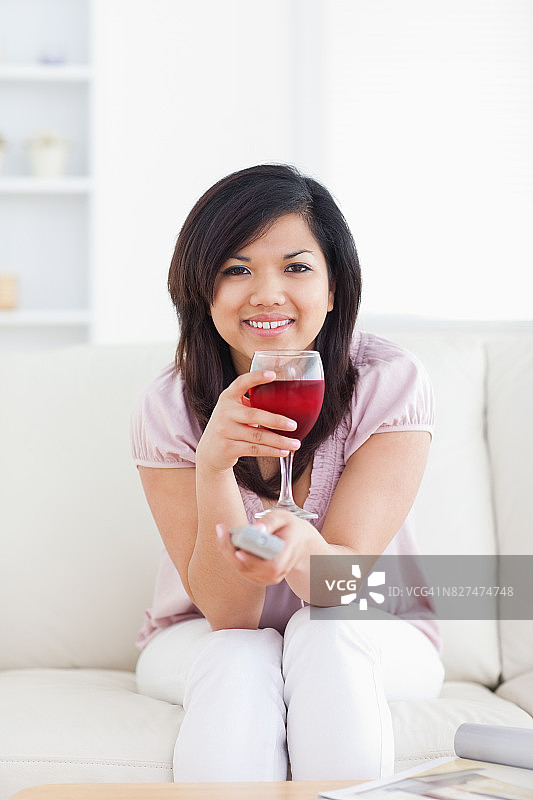 拿着电视遥控器的女人手里拿着一杯红酒图片素材