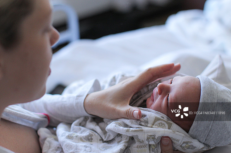 一位年轻的妇女把她刚出生的婴儿紧紧地攥在手里，以减轻他的压力。图片素材