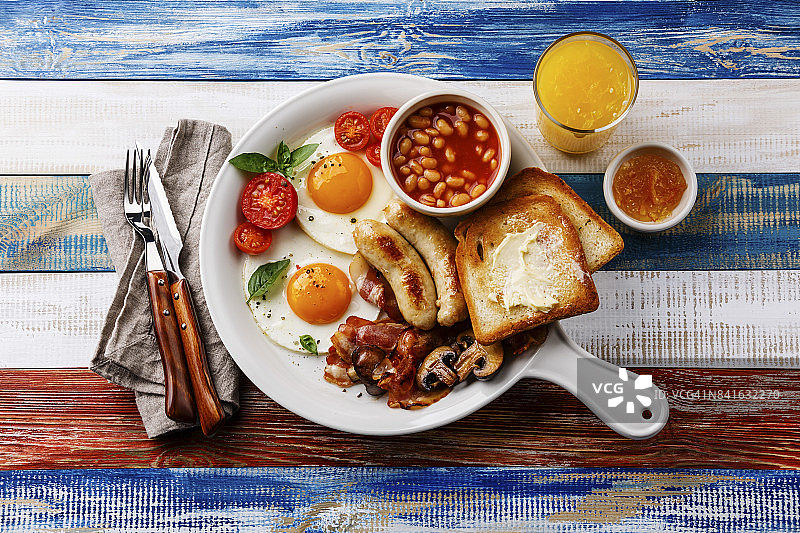 白色平底锅里的英式早餐，配上煎蛋、香肠、培根、豆类、吐司和鲜橙图片素材