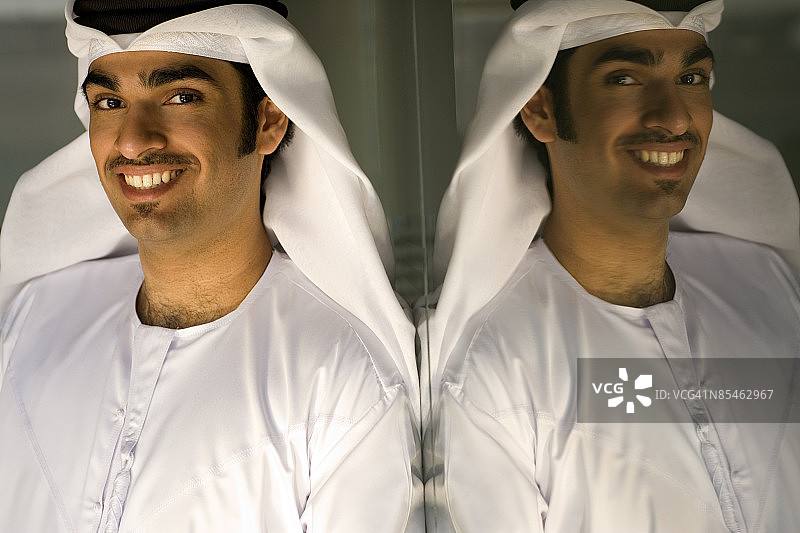 一个阿联酋男人的侧面和他在玻璃墙上的倒影。图片素材
