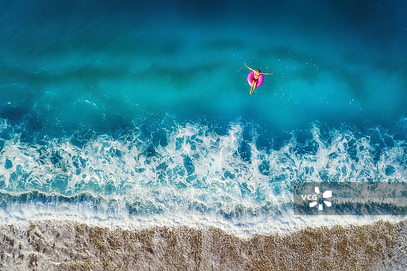 鸟瞰图上的年轻女子游泳在粉红色的游泳圈在透明的绿松石海Oludeniz，土耳其。夏天的海景与少女，美丽的海浪，蔚蓝的水在日落。无人机俯视图图片素材
