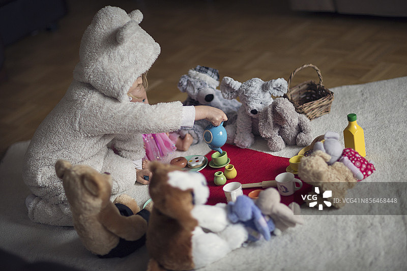 孩子穿着舒适的连帽熊服装，和泰迪熊和洋娃娃一起开茶话会图片素材
