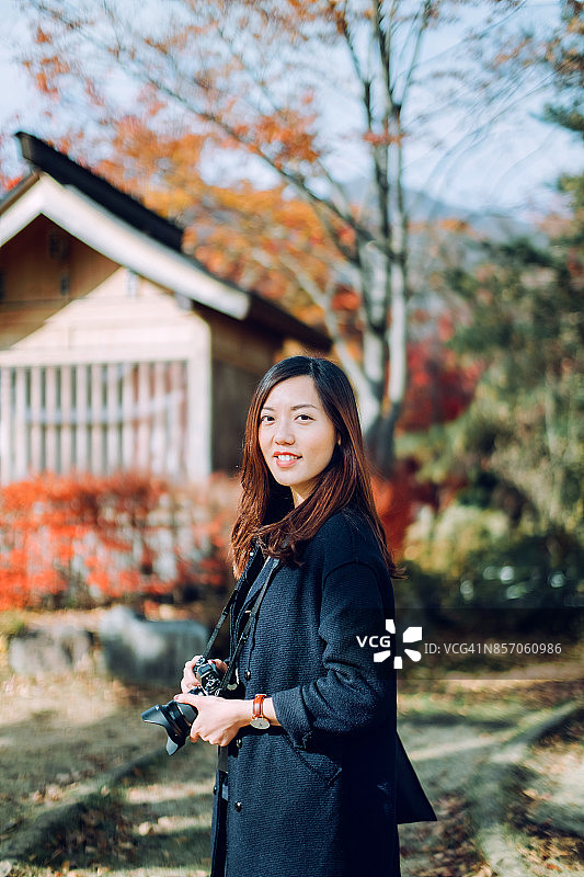 微笑的亚洲女游客用相机在公园里拍摄美丽的秋叶图片素材