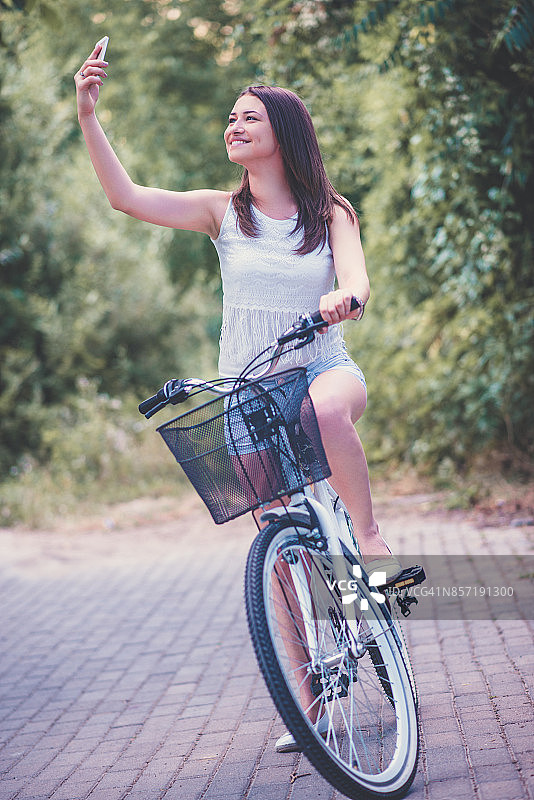 可爱的微笑女性在城市公园骑车自拍图片素材