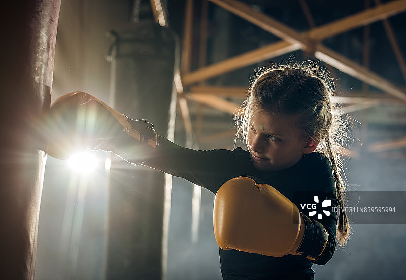 一个小女孩在健身俱乐部拳击训练中打一个袋子。图片素材