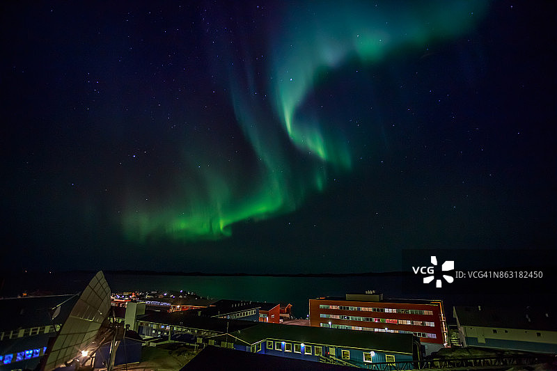 北极光的绿色灯光与闪烁的星星在夜晚的海湾和突出的建筑努克市，格陵兰图片素材