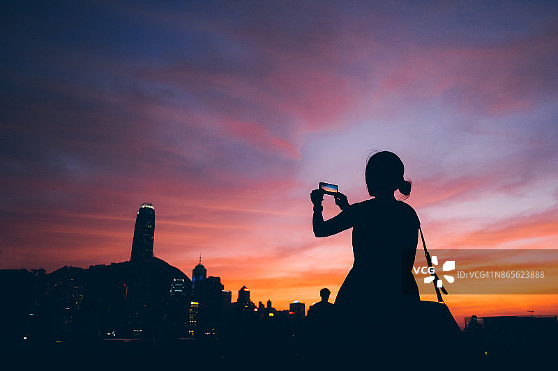 剪影的女人拍照美丽的日落在城市上空图片素材