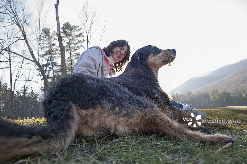 成年妇女坐在草地上，她的狗在她旁边图片素材