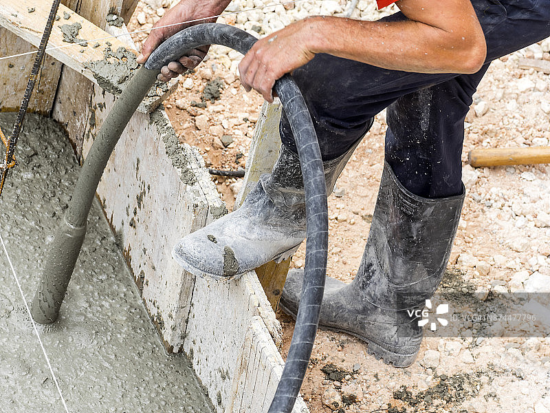 一个建筑工人在建筑工地工作的高角度视图，与一个软管在手上正在与混凝土工作，西班牙图片素材