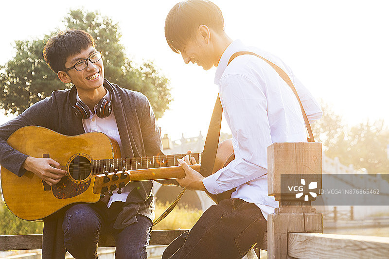 两个男人，朋友在桥的木栏杆上弹吉他图片素材