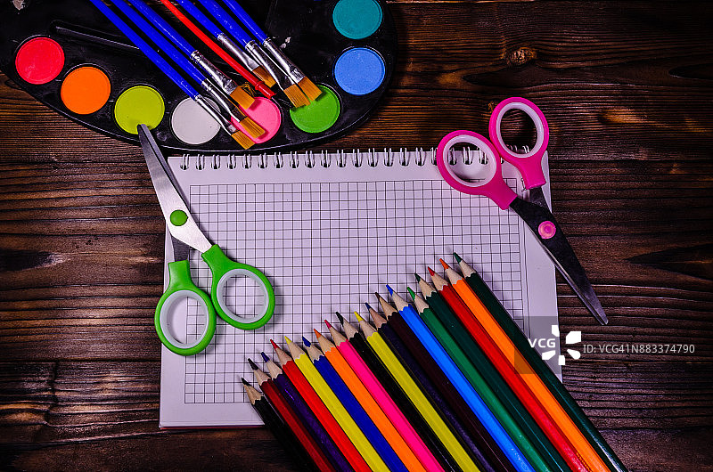 一套不同的文具。笔记本，剪刀，铅笔，颜料，画笔放在木桌上。回到学校。俯视图图片素材