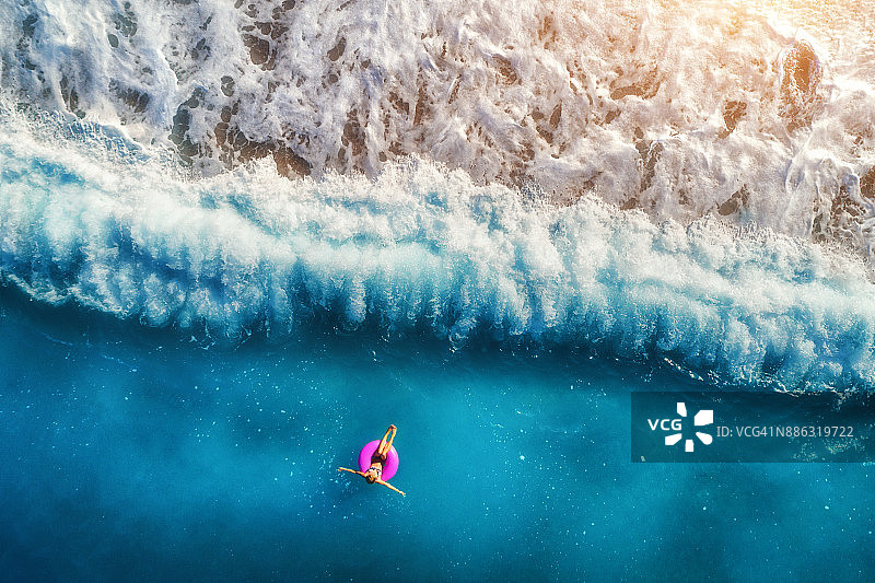 鸟瞰图上的年轻女子游泳在粉红色的游泳环在透明的绿松石海在Oludeniz。夏天的海景，沙滩，美丽的海浪，蓝色的水在日落。无人机俯视图图片素材