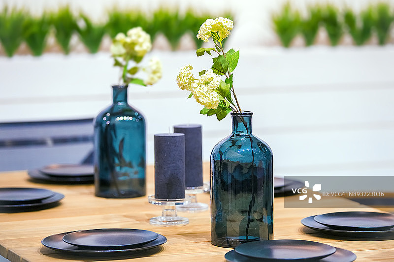 桌子上放着黑色的盘子，玻璃花瓶上插着鲜花。餐桌上的装饰图片素材