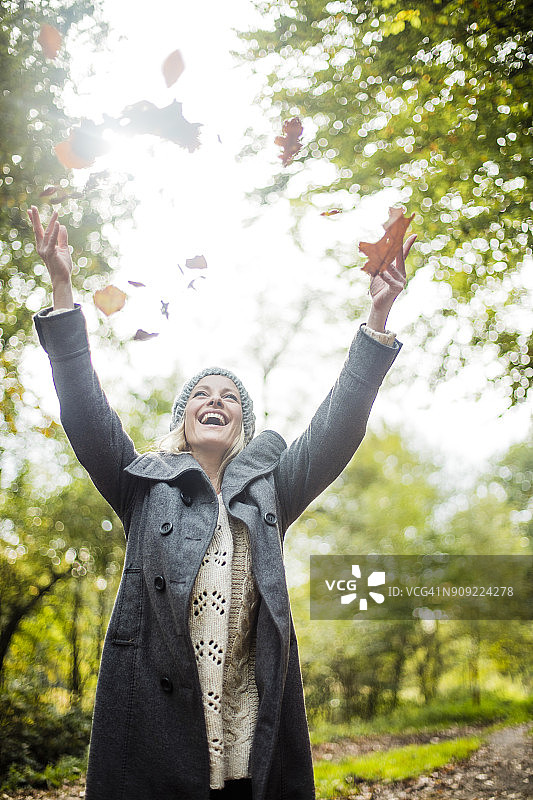 快乐的女人在秋天的森林里把树叶抛向空中图片素材
