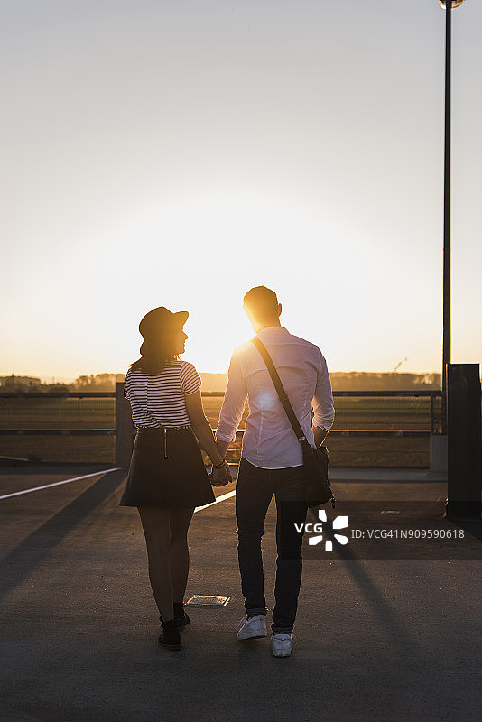 日落时分，一对年轻夫妇手牵手在停车场上散步图片素材
