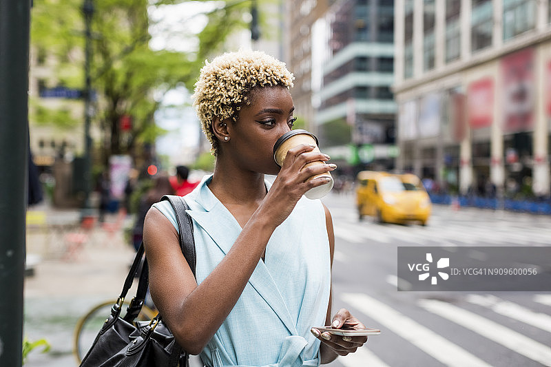 美国，纽约，年轻的金发非洲裔美国女人拿着咖啡杯和智能手机图片素材