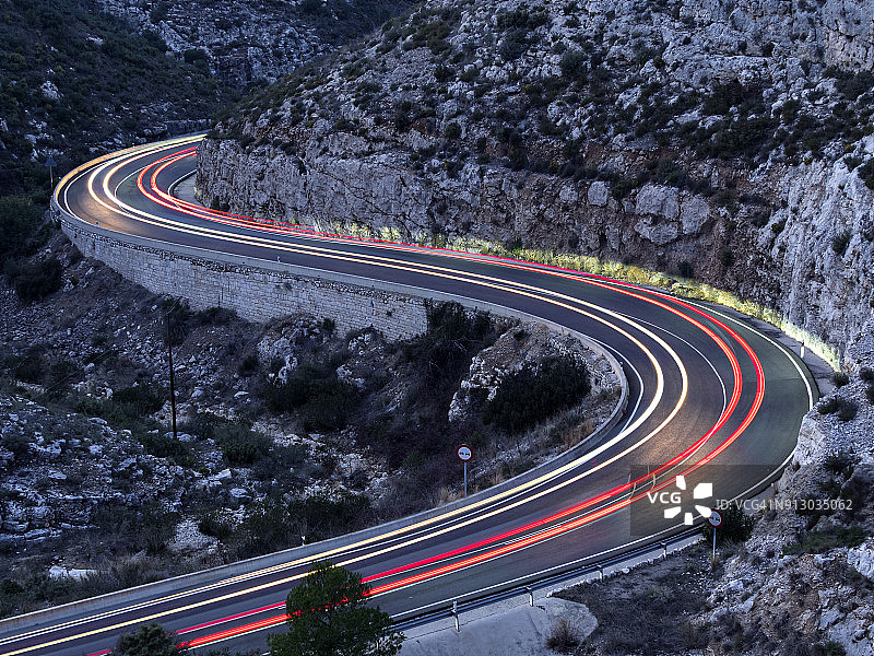 灯光和车辆的痕迹，汽车和卡车，在山谷之间的山路上循环，在夜晚封闭的圆形弯道。瓦伦西亚,西班牙图片素材