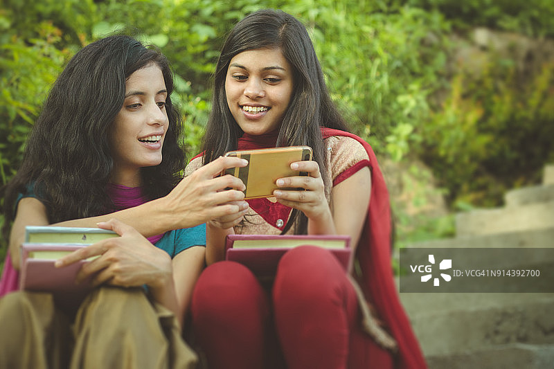 两名来自农村的印度女大学生分享智能手机。图片素材