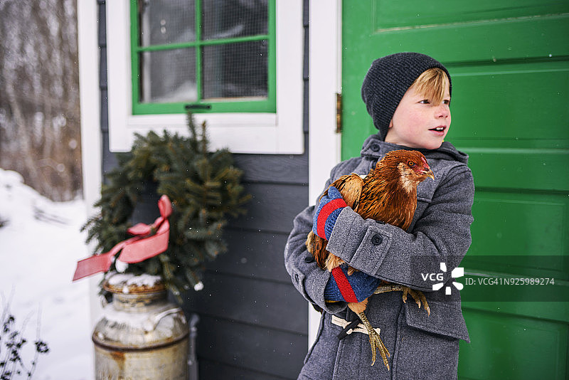 一个男孩站在房子外面，手里拿着一只鸡图片素材