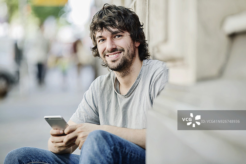 一个在户外拿着手机微笑的年轻人的肖像图片素材