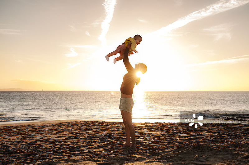 日落时分，母亲在海滩上抱起小女儿图片素材