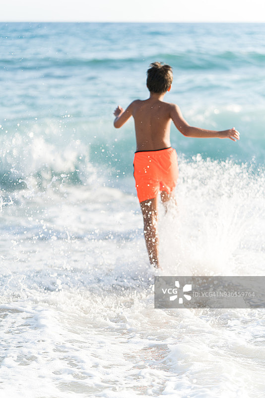 年轻的男孩在海滩上跑在水里图片素材