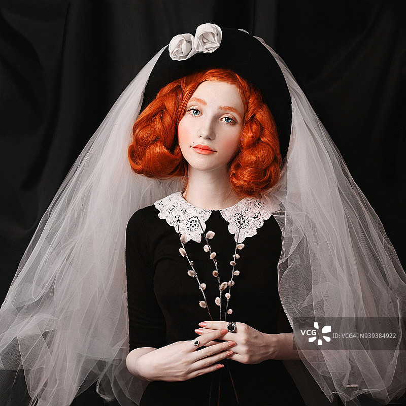 维多利亚时代的一名红发妇女，梳着长长的辫子，穿着黑色的连衣裙，头戴面纱。可爱的女孩苍白的皮肤和戒指上的石头在黑色的背景。图片素材