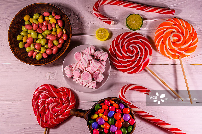 瓷碗，木桌上放着彩色糖果、棒棒糖和棉花糖。俯视图图片素材